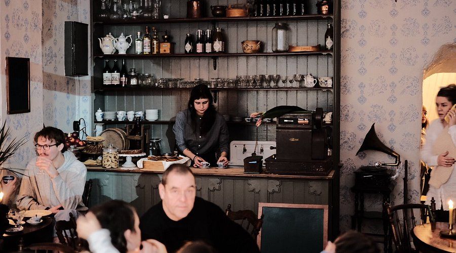 Interiör av ett rustikt café med gäster och en stor trähylla på Södermalm.
